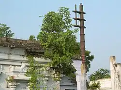 Side view showing Dhwajasthambham and wall with plants growing on it