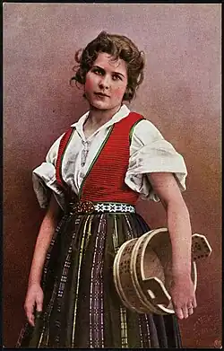 Kvinne i nasjonaldrakt holder en tine under armen