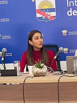 Larissa Rú sits behind a table with microphones at the 2022 Feria De Promoción De La Lectura y El Libro in Uruguay