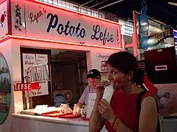 chest high portrait of a woman customer eating in front of neon-lit Lynn's Potato Lefse stand