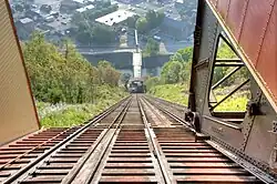 The Johnstown Inclined Plane's tracks as seen from the upper station. The trackbed is made of wood. The lower station is visible in the background, and the Inclined Plane Bridge crosses the Stoneycreek River behind the lower station.