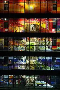 An illuminated, colorful mural painting distributed across the galleries and interior staircase along the five-floor facade of the interior courtyard of an office building