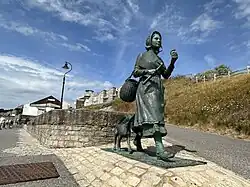 A bronze statue of Mary Anning striding forward, with a pickaxe in one hand and a fossil in the other.