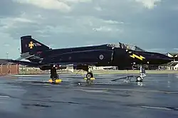 Side view of a Phantom FG.1. The aircraft is painted all over black with a yellow lightning flash on the nose and a yellow cross potent quadrat on the tail. this marking represents Treble-One Squadron