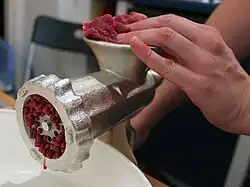 table top machine with handle, meat is inserted in a top aperture and emerges minced from the side aperture