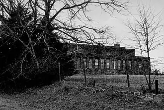 An abandoned church building behind an overgrowth of trees and a fence.