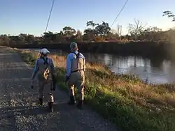 Two people walking along the river.