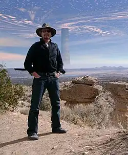 Michael Whelan poses with the Dark Tower photo-edited into the background with clouds swirling overhead
