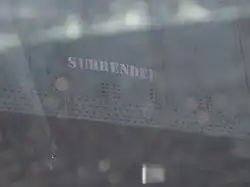 Miniature SURRENDER graffiti from 2007 stenciled on the green railroad bridge. Above the stencil are dark green squares where the previous graffito has been painted over.