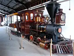 A red steam locomotive with a 0-4-2T wheel arrangement (no leading wheels, four driving wheels, and two trailing wheels) and no tender, coupled to a small train car