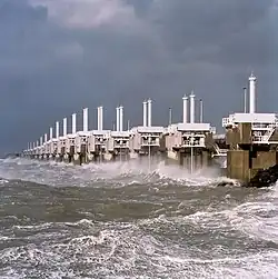 A long row of concrete towers with steel structures connecting them and a very rough sea