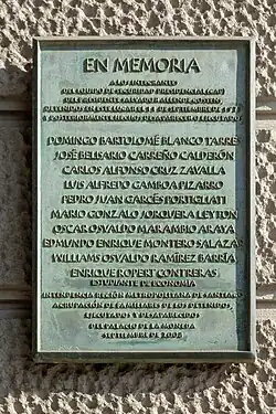 A color, close-up photograph of a plaque fixed to the side of a building. The plaque is lettered in Spanish. At the top are the word "En Memoria" ("in memory of"). Below this is a list of names.