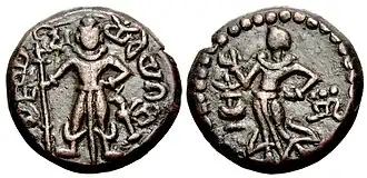 Yaudheya coin, imitative of Kushan coinage, 3rd-4th centuries CE. Obverse: Karttikeya standing facing, holding a spear with dvi (“two” in Brahmi) to the left of Karttikeya's head, peacock to lower right, Brahmi legend around: 𑀬𑁅𑀥𑁂𑀬 𑀕𑀦𑀲𑁆𑀬 𑀚𑀬 (yaudheya ganasya jaya, “Victory to the Yaudheya people”). Reverse: Devasena standing left, raising hand; flower vase to left, inverted nandipada to the right.[1] of