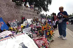 Mourners lay flowers and tributes in front of the Reagan Library's sign.