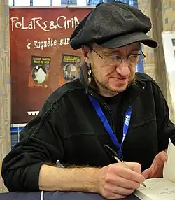 Marhic signing books in front of an advertisement for his books