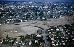 Aerial view of a suburban neighborhood with a diagonal swath cleared of homes and turned into dirt. A few roads cross over the dirt trench.