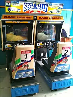 An arcade cabinet with two seats and steering wheels