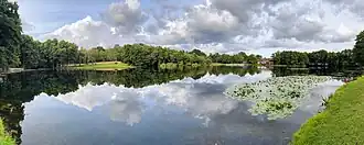 A small lake surrounded by trees with a large house on the far side