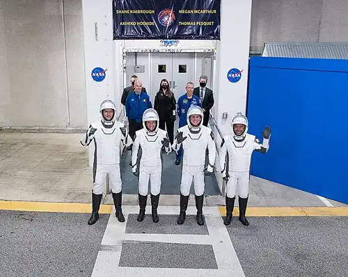 Photo of Crew-2 astronauts waving from an elevator of the Neil Armstrong Operations and Checkout Building