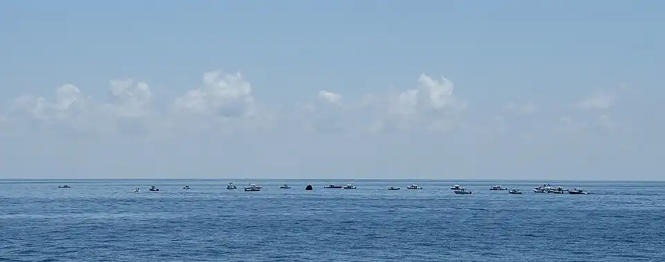 Large numbers of private boats create a circle around the Endeavour capsule.