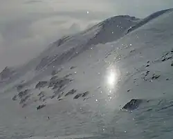 A more vertically elongated subsun before a gentle, snow-covered cliff