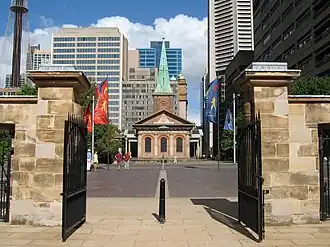 A recent photo. The church is seen framed by the gateposts of the nearby Barracks. Its steeple is seen against a backdrop of multi-storey buildings.