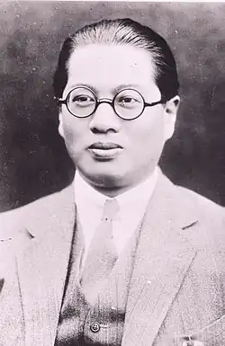 A Chinese man wearing round glasses and a western-style business suit
