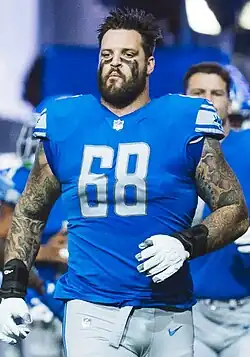 Taylor Decker in a Detroit Lions uniform without the helmet. His face is painted and he's shown from about the thighs up.