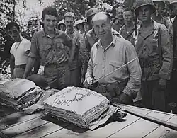 William W. Stickney cuts a Thanksgiving cake with a Japanese officer's sword at Guadalcanal, as hungry Leathernecks look on