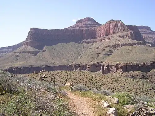 View of Tower of Set peak and sub-unit cliff section from Tonto Trail, Granite Gorge, north of Mohave Point, Grand Canyon Village, South Rim. The peak is behind and separated from a cliff unit (with small prominence), in front-(photo center, right, Tower of Set (peak) to its left). Vertical erosion in cliff of Redwall Limestone, upon horizontal Muav Limestone cliff.[19] The Tapeats Sandstone sits in foreground on Granite Gorge, and is seen as thinly-bedded. The slope-former above is the (dull-greenish)-Bright Angel Shale with thin, inter-bedding, as well as one resistant cliff unit. The Redwall Limestone cliff section in Grand Canyon is about 450 feet (137 m) thick.[20]