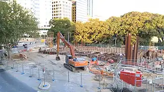 Construction site with an excavator sitting there. The station box has begun to be excavated.
