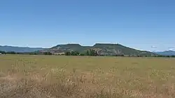 Upper Table Rock from across a field of grass, looking into the central bowl. It rises steeply from the surrounding valley to its flat top.