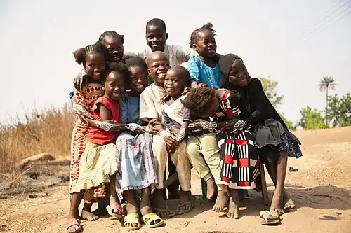 Photo of a group of children that are sitting outside, smiling, and laughing