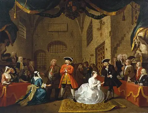 A group of characters stands in a stone room. Two women kneel before two men pleadingly. A man in a red coat stands on watching them, wearing chains on his legs. The whole scene is surrounded by a theatrical curtain.