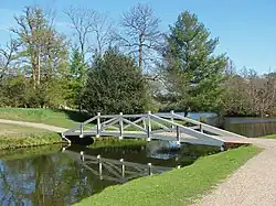 A colour photograph of a wooden bridge painted white crossing a narrow water-filled channel