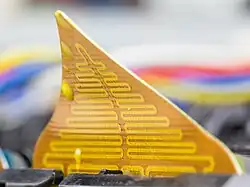 a bent brown kapton triangle with gold zigzag circuit traces and droplets of hardened yellow wax