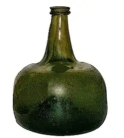 A squat semi-transparent green blown glass bottle, shaped vaguely like a squarish mandarin citrus, with a strongly concave base and a short flanged neck.