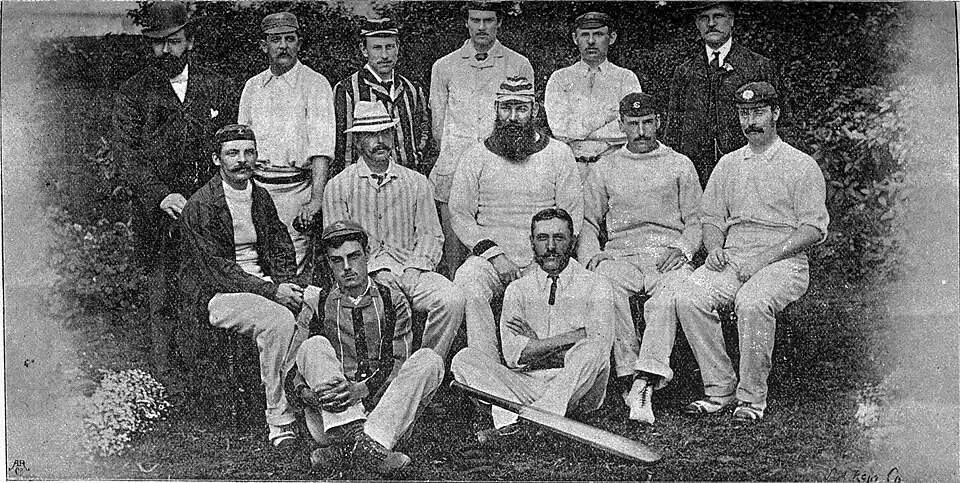 11 men dressed in cricket clothing posing for a group photograph. Three rows.