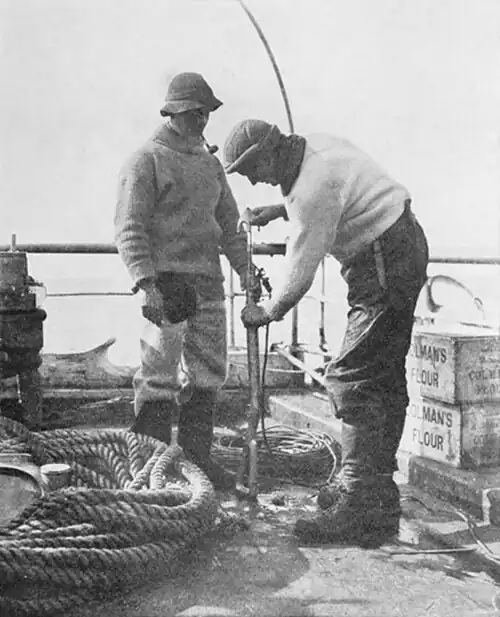 Photograph of two men on the deck of a ship with a harpoon rifle