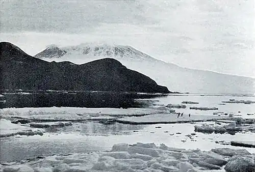 Photo of a bay with ice floes, a bare hilly cape, and a cloud-bound mountain