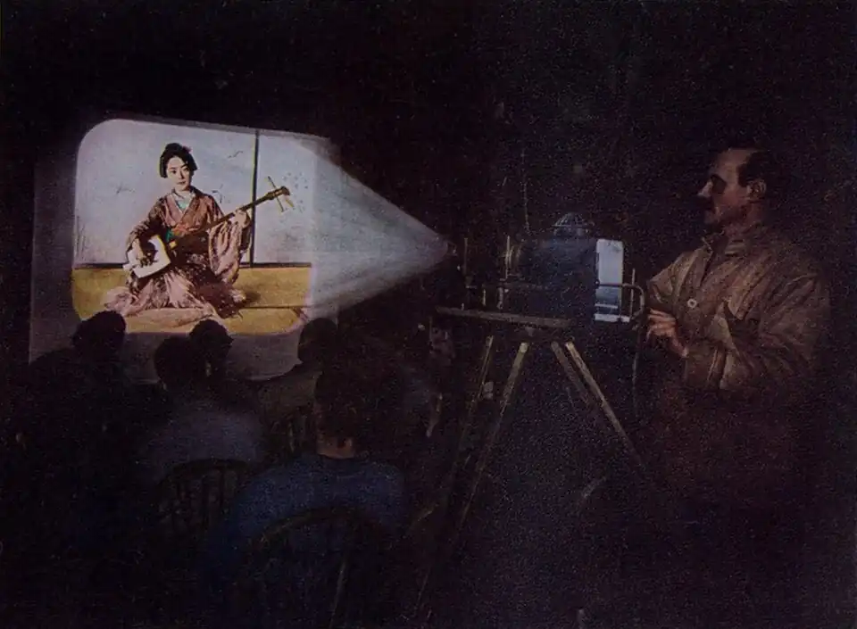 Watercolour painting of a man projecting an image of a Japanese woman playing a shamisen for a small seated audience