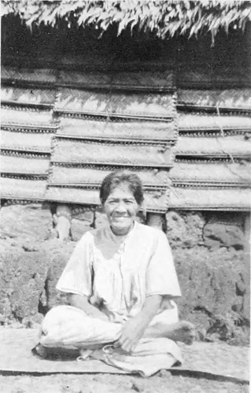 A photo of a woman seated in front of a building