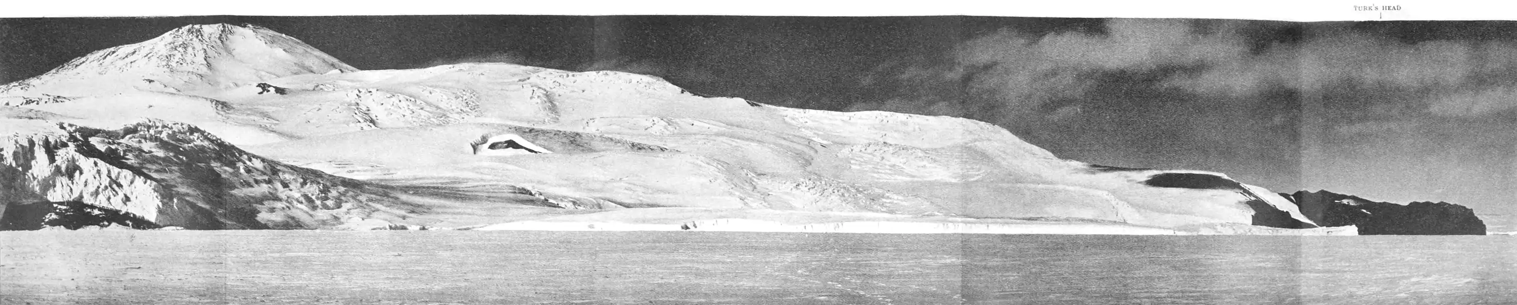 Fold-out panoramic photo of sprawling, bay-side mountain with a snow-free headland at the far right