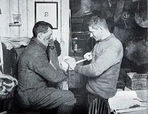 Photo of a man wrapping tape around the hand of a pipe-smoking man with dark bruising on his face
