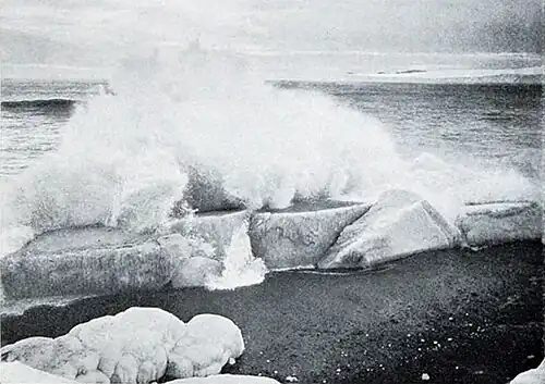 Photo of a big spray of water over a slab of ice on shore