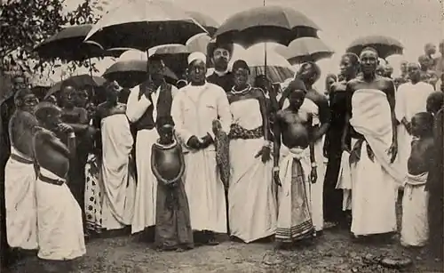 A large group standing, many in white robes, and several with parasols