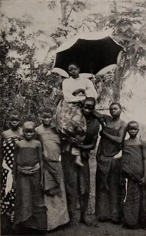 A crowd with a woman held on a person's shoulder and another person holding up a parasol over her head
